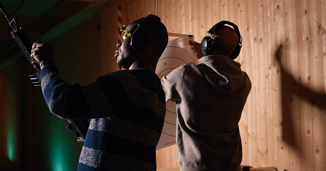Un homme tient un fusil et profite d'une séance de tir récréative dans un stand de tir, entouré d'un groupe d'amis. Des personnes s'entraînent au maniement des armes dans un environnement sécurisé au sein d'un stand de tir.